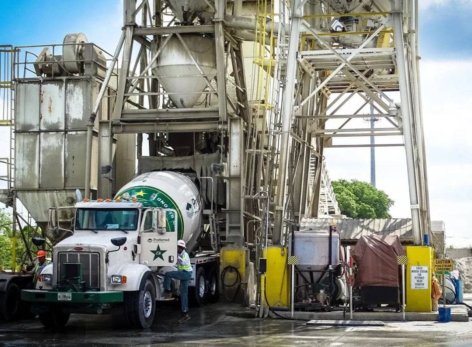 A cement truck parked in front of a large concrete plant.