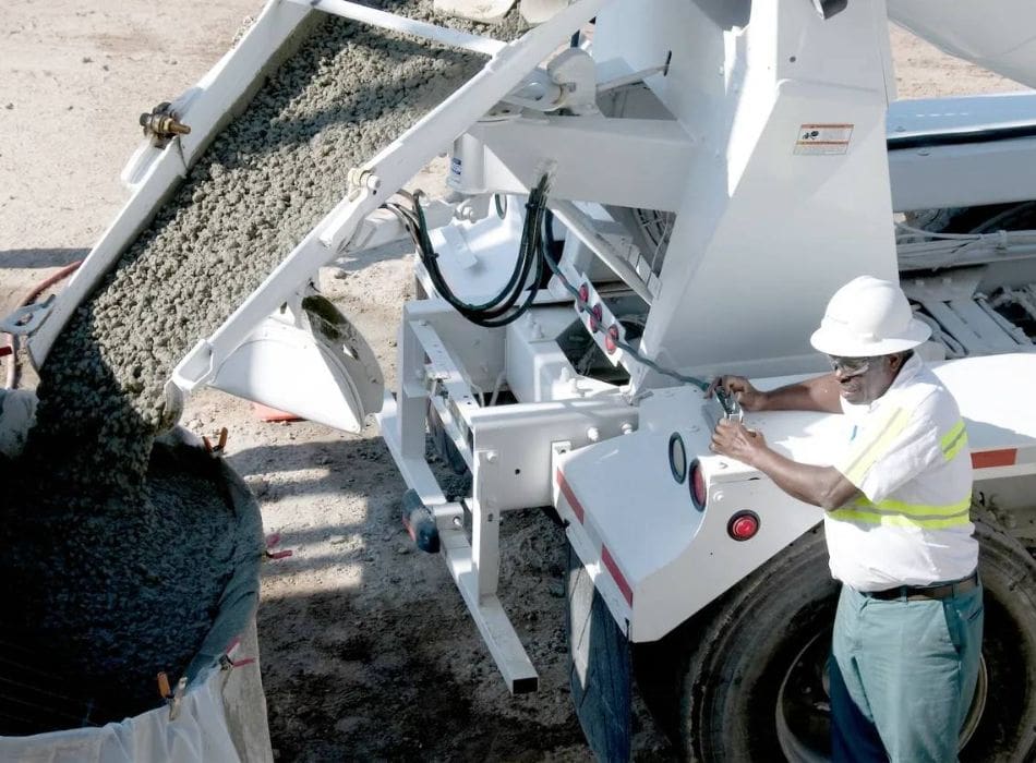 A man in white hard hat standing next to a concrete mixer.