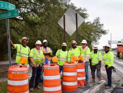 A group of construction workers standing next to orange barrels.